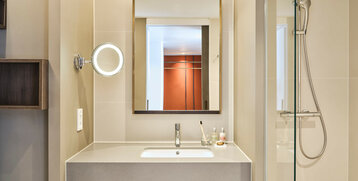 Modernes Hotelbad mit Waschbecken, beleuchtetem Spiegel und Regendusche im ATLANTIC Hotel Münster.