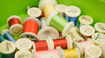 Upcycling Initiative | ATLANTIC Hotel Sail City Bunte Garnrollen in einer grünen Box, symbolisieren Kreativität und Handwerkskunst im ATLANTIC Hotel Sail City.
