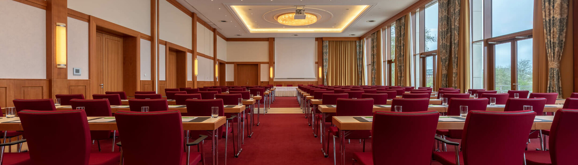 Veranstaltungsraum Wilhelmshaven | ATLANTIC Hotel Wilhelmshaven Konferenzraum mit roten Stühlen, Tischen, großen Fenstern und eleganter Beleuchtung im ATLANTIC Hotel Wilhelmshaven.