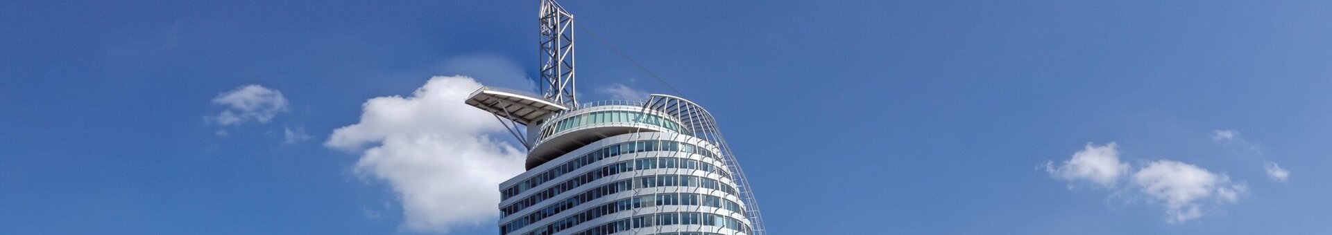 Außenansicht ATLANTIC Hotel Sail City am Weserdeich in Bremerhaven Modernes Hochhaus des ATLANTIC Hotel Sail City in Bremerhaven, direkt am Wasser mit blauem Himmel im Hintergrund.