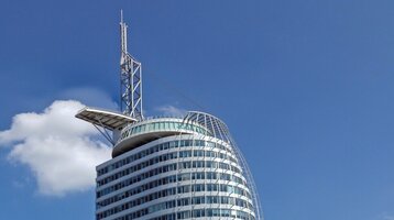 Modernes Hochhaus des ATLANTIC Hotel Sail City in Bremerhaven, direkt am Wasser mit blauem Himmel im Hintergrund.