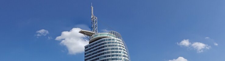 Modernes Hochhaus des ATLANTIC Hotel Sail City in Bremerhaven, direkt am Wasser mit blauem Himmel im Hintergrund.