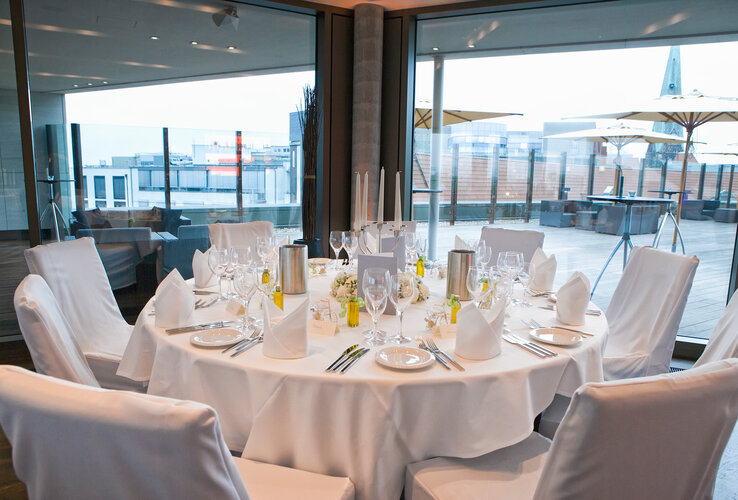 Eleganter, gedeckter runder Tisch im ATLANTIC Grand Hotel Bremen mit Stadtblick durch große Fenster.