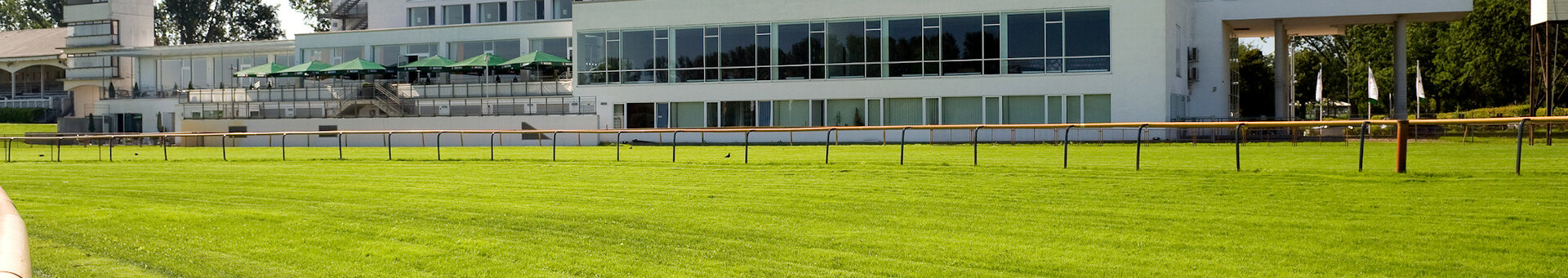 ATLANTIC Hotel Galopprennbahn, modernes Gebäude mit großen Fenstern, umgeben von grünem Rasen und Bäumen.