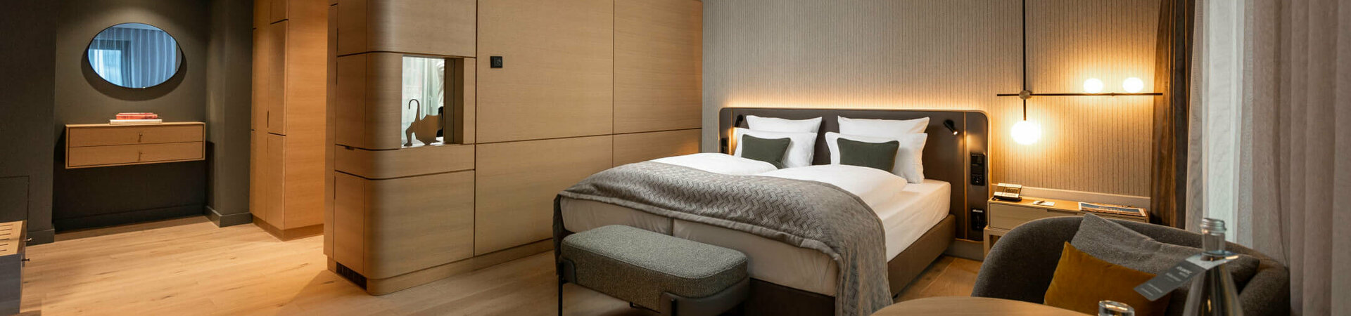 Modernes Hotelzimmer mit Doppelbett, Holzinterieur, gemütlicher Beleuchtung und Sitzbereich im ATLANTIC Hotel Heidelberg.