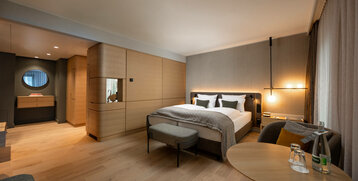Modernes Hotelzimmer mit Doppelbett, Holzinterieur, gemütlicher Beleuchtung und Sitzbereich im ATLANTIC Hotel Heidelberg.