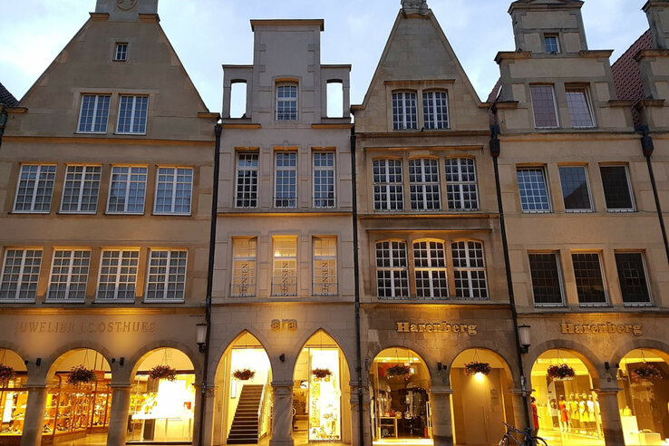 Historic facades with illuminated arcades and stores in Münster at dusk.