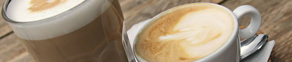 Ein Latte Macchiato und Cappuccino mit Keksen auf einem Holztablett.