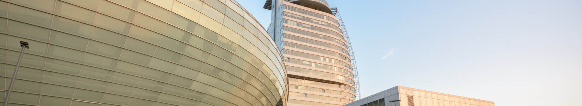 Arrival and location at the ATLANTIC Hotel Sail City ATLANTIC Hotel Sail City in Bremerhaven, modern high-rise building with curved glass façade and adjoining conference center.