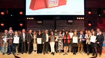 Eine Gruppe von Menschen auf einer Bühne hält Urkunden, darüber ein Banner mit "Tourismus Preis 22 Bremen Bremerhaven".