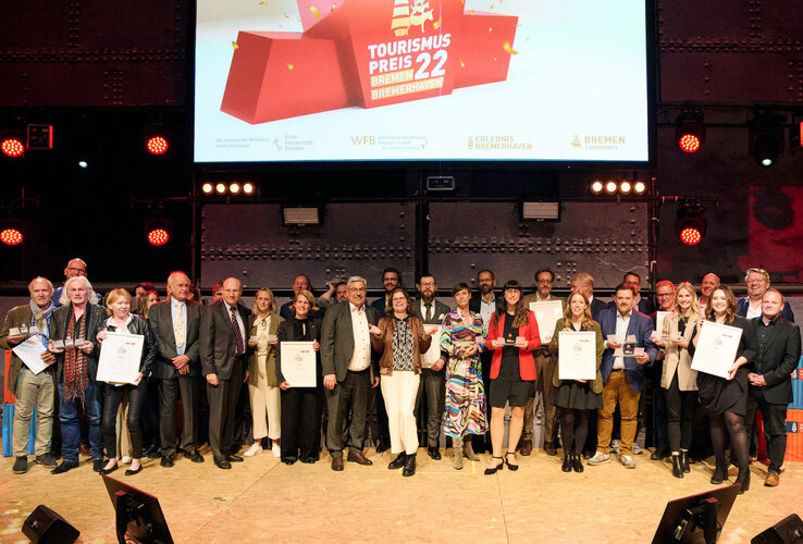 A group of people on a stage holding certificates, above them a banner with "Tourismus Preis 22 Bremen Bremerhaven".