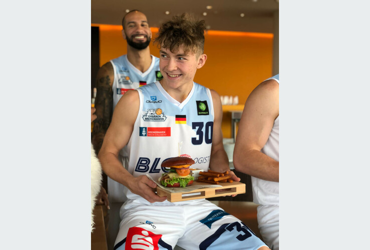 Basketball player in jersey holds tray with burger and fries in the ATLANTIC Hotel Sail City.