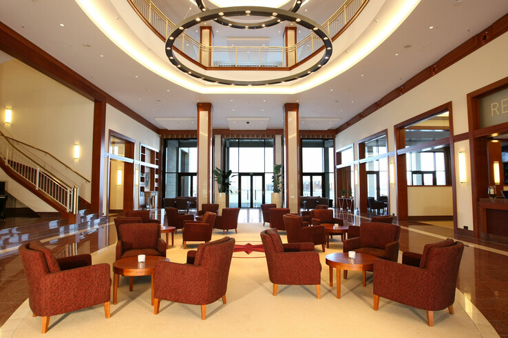 Geräumige Hotel-Lobby mit roten Sesseln, runden Tischen, großen Fenstern und eleganter Beleuchtung.