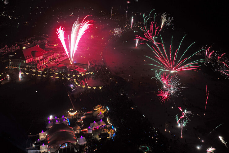 Feuerwerk über dem ATLANTIC Grand Hotel Travemünde bei Nacht, mit Menschenmengen und beleuchteten Zelten im Vordergrund.