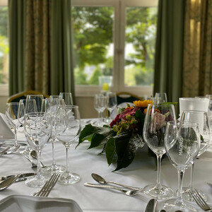 Hochzeit im ATLANTIC Hotel Landgut Horn Eleganter, gedeckter Tisch mit Blumenarrangement vor großen Fenstern im ATLANTIC Hotel Landgut Horn Bremen.