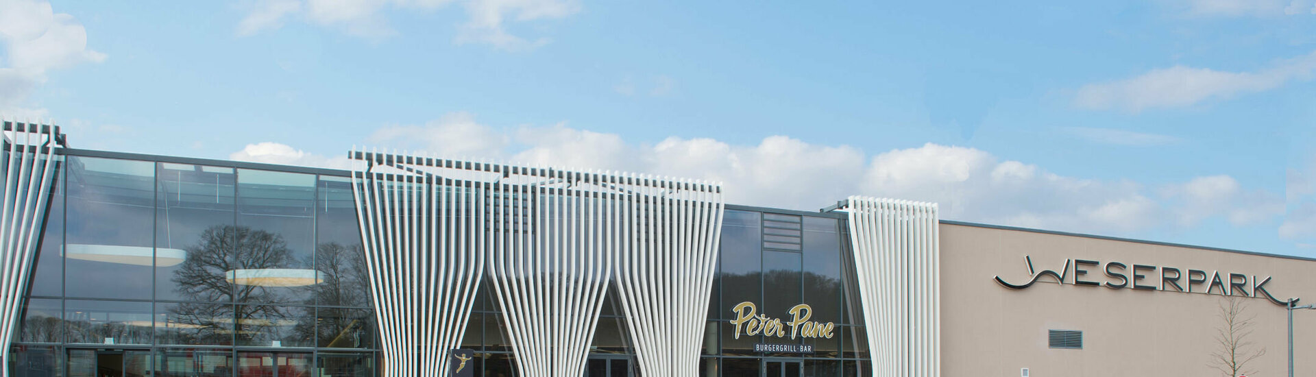 Weserpark Bremen Eingang des Weserparks mit modernem Glasdesign, Menschen und Autos auf dem Vorplatz bei sonnigem Wetter.