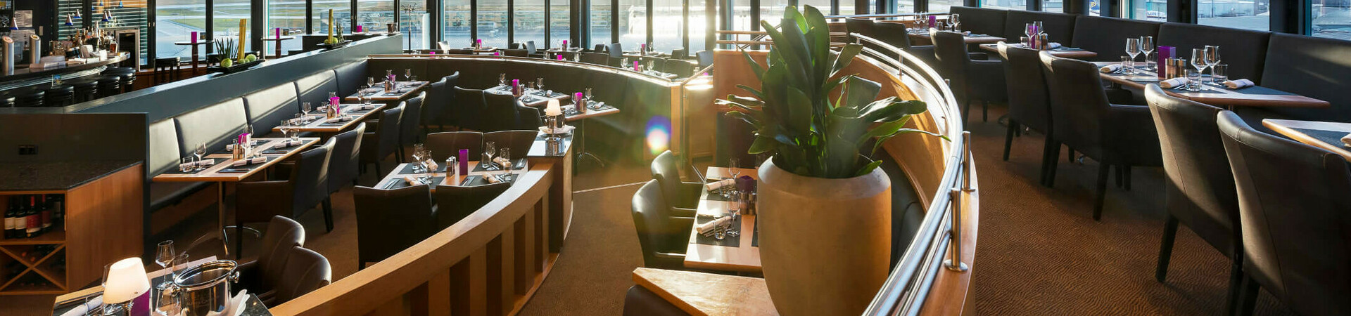Modernes Restaurant im ATLANTIC Hotel Airport Bremen mit Panoramafenstern, stilvoll gedeckten Tischen und eleganter Beleuchtung.