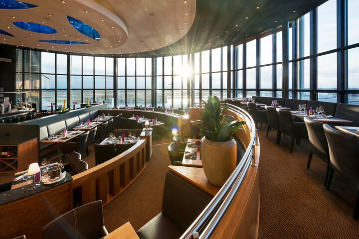 Modernes Restaurant im ATLANTIC Hotel Airport Bremen mit Panoramafenstern, stilvoll gedeckten Tischen und eleganter Beleuchtung.