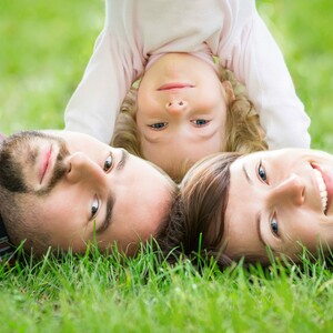 A family and their child are lying on a meadow next to the ATLANTIC Hotel Gal A family lies smiling on the lawn, a child stands upside down between the parents.