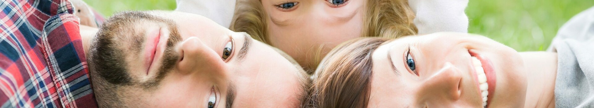 A family lies smiling on the lawn, a child stands upside down between the parents.