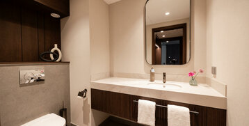 Modernes Badezimmer mit großem Spiegel, Waschbecken, dekorativen Blumen und Handtüchern im ATLANTIC Hotel Heidelberg.