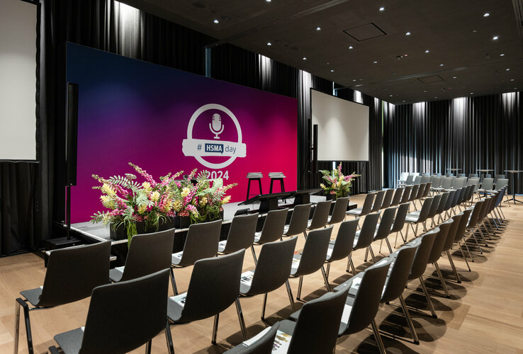 Moderner Konferenzraum mit Bühne, Stühlen und Blumenarrangement im ATLANTIC Hotel Heidelberg.