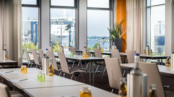Heller Konferenzraum im ATLANTIC Hotel Kiel mit Tischen, Stühlen, Getränken und Blick auf den Hafen.