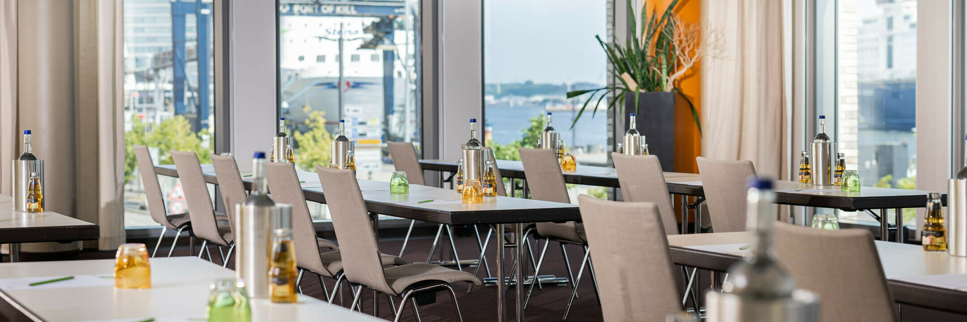 Heller Konferenzraum im ATLANTIC Hotel Kiel mit Tischen, Stühlen, Getränken und Blick auf den Hafen.