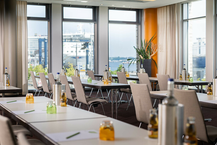 Heller Konferenzraum im ATLANTIC Hotel Kiel mit Tischen, Stühlen, Getränken und Blick auf den Hafen.