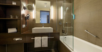 Modernes Badezimmer im ATLANTIC Hotel Lübeck mit Waschbecken, Spiegel, Badewanne und Handtüchern.