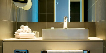 Modern bathroom in the ATLANTIC Hotel Sail City with washbasin, mirror and stacked towels.