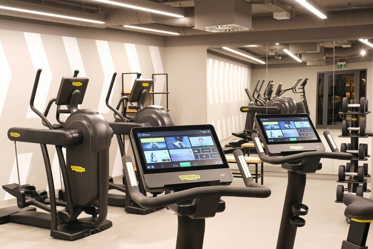 Modern fitness room at the ATLANTIC Hotel Münster with treadmills, screens and weights.