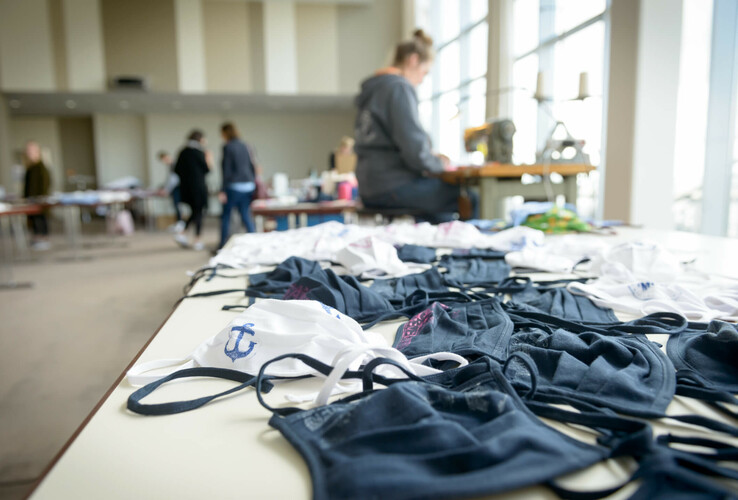 Stoffmasken auf einem Tisch im ATLANTIC Hotel Sail City, Bremerhaven, mit Menschen im Hintergrund.