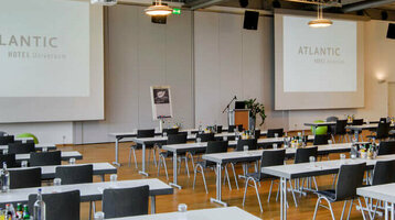 Modern conference room in the ATLANTIC Hotel Universum with tables, chairs and large windows.