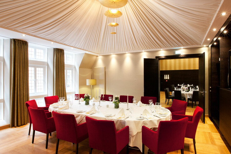 Eleganter Speisesaal mit rundem Tisch, roten Stühlen und stilvoller Beleuchtung unter einem drapierten Deckenstoff.