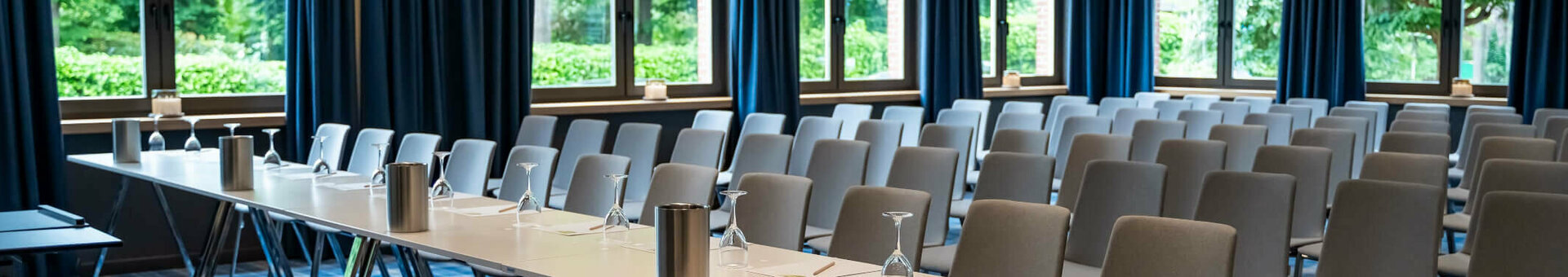 Moderner Konferenzraum mit blauen Vorhängen, Tischen und Stühlen im ATLANTIC Hotel Landgut Horn Bremen.