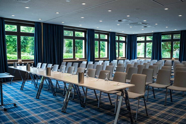 Moderner Konferenzraum mit blauen Vorhängen, Tischen und Stühlen im ATLANTIC Hotel Landgut Horn Bremen.