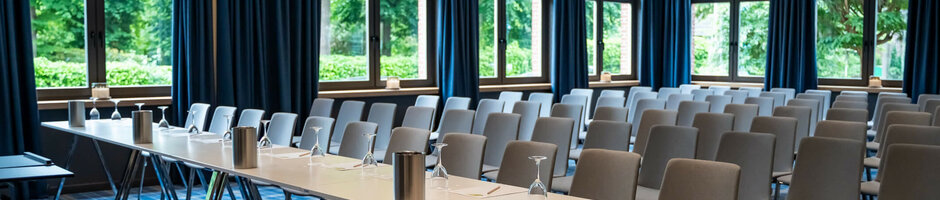 Modern conference room with blue curtains, tables and chairs at the ATLANTIC Hotel Landgut Horn Bremen.