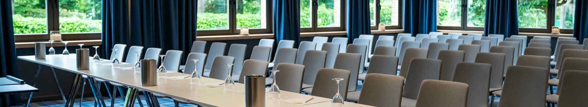Moderner Konferenzraum mit blauen Vorhängen, Tischen und Stühlen im ATLANTIC Hotel Landgut Horn Bremen.