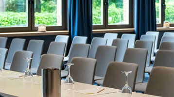 Moderner Konferenzraum mit blauen Vorhängen, Tischen und Stühlen im ATLANTIC Hotel Landgut Horn Bremen.