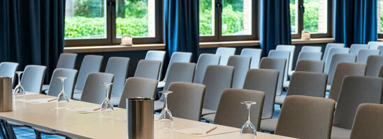 Moderner Konferenzraum mit blauen Vorhängen, Tischen und Stühlen im ATLANTIC Hotel Landgut Horn Bremen.