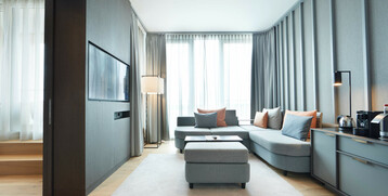 Bright hotel room with gray sofa, pillows, carpet, flat-screen TV and coffee machine at the ATLANTIC Grand Hotel Bremen.