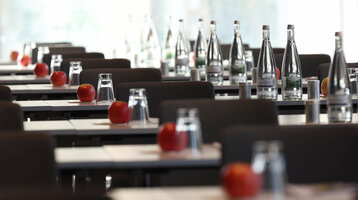 Reihen von Konferenztischen mit Wasserflaschen, Gläsern und roten Äpfeln im ATLANTIC Hotel Heidelberg.