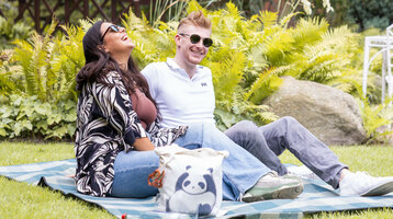 ATLANTIC Hotel Landgut Horn Angebote im Grünen  Ein Paar sitzt auf einer Picknickdecke im grünen Garten vom ATLANTIC Hotel Landgut Horn