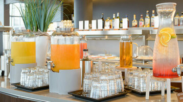 Getränkestation im ATLANTIC Hotel Sail City mit Saftspendern, Gläsern und modernem Interieur.