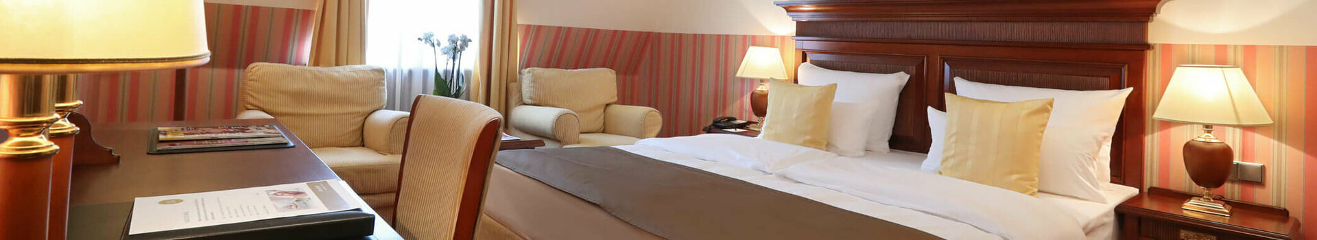 ATLANTIC Grand Hotel Travemünde Doppelzimmer Standard klassisch Gemütliches Hotelzimmer mit Doppelbett, Holzmöbeln, Sesseln, warmem Licht und Blumenbild an der Wand.