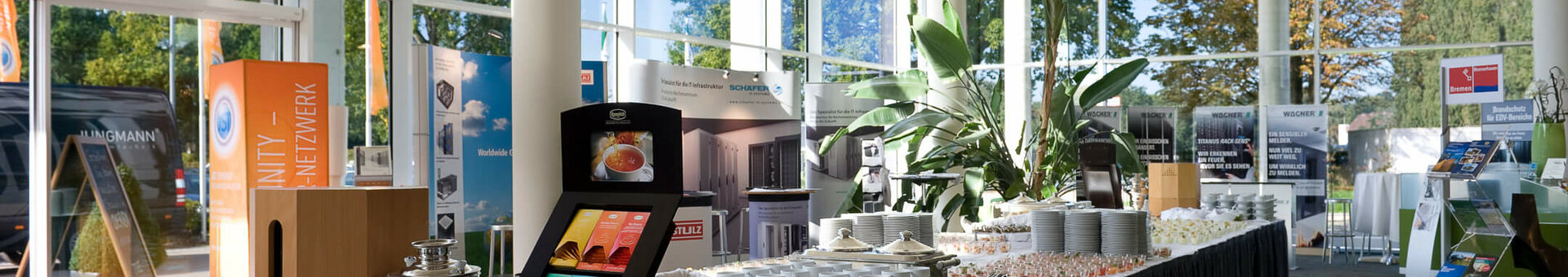 Catering in der Lobby vom ATLANTIC Hotel Galopprennbahn Helles Frühstücksbuffet mit Gebäck, Tee und Geschirr im ATLANTIC Hotel Galopprennbahn, umgeben von großen Fenstern und Pflanzen.