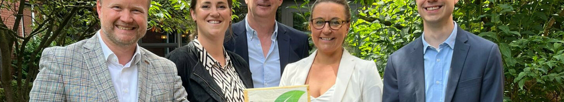 Pressemitteilung | ATLANTIC Hotels Gruppe GreenSign zertifiziert Fünf Personen lächeln in einem Garten, halten ein "Greensign Hotel"-Schild.