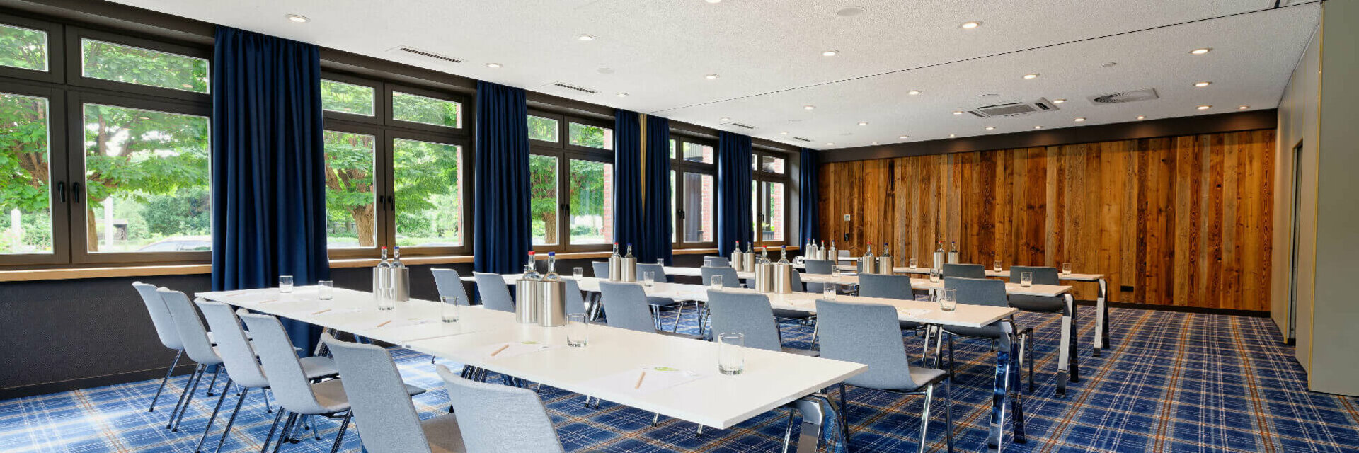 Heller Konferenzraum mit blauen Teppich, weißen Tischen und grauen Stühlen im ATLANTIC Hotel Landgut Horn Bremen.