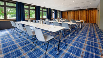Heller Konferenzraum mit blauen Teppich, weißen Tischen und grauen Stühlen im ATLANTIC Hotel Landgut Horn Bremen.